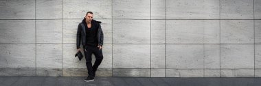 Gri duvara yaslanmış siyah elbiseli bir adam. Fotokopi alanı olan modern ve şehir tarzı. Moda ya da yaşam tarzı promosyonları için ideal.