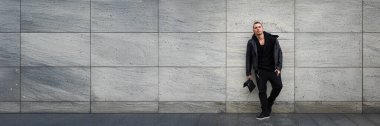 Siyahlı şık bir adam gri bir duvara karşı, kopyalama alanı olan minimalist tarzda. Moda, yaşam tarzı veya kentsel temalı ticari kullanım için ideal.