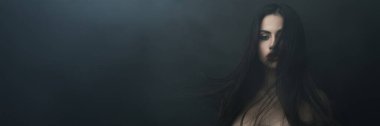Huysuz bir arka planda uzun, koyu renk saçlı bir kadının büyüleyici portresi. Geniş bir pankartta güzellik, moda ve editoryal içerik için mükemmel.