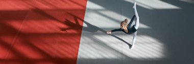 Genç bir jimnastikçi renkli bir paspasın üzerinde çift atlama yapıyor. Görüntü parlak ve dinamik, spor etkinlikleri veya jimnastik dersleri için ideal. Kopyalama alanı olan geniş pankart.
