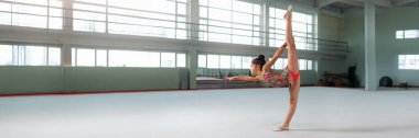 Geniş bir spor salonunda poz veren genç bir jimnastikçi. Dengeli, renkli ve dinamik, geniş bir kopya alanı var. Spor ve spor reklamları için ideal..