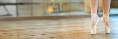 Stüdyoda sivri uçlu ayakkabı giyen balerin yakın çekimi. Sıcak tonlar ve zarif kompozisyon. Fotokopi alanı ile dans promosyonları için ideal. Geniş pankart biçimi.