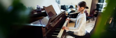 Parlak bir odada piyano çalan genç bir kız, sakin ve odaklanmış bir atmosfer yaratıyor. Geniş pankart biçimi, kopyalama alanı ile ticari kullanıma izin verir.