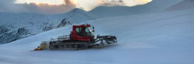 Mavi arkaplanı olan karlı bir dağda kızıl bir kar temizleyicisi. Kış, seyahat ve açık hava teması için idealdir..