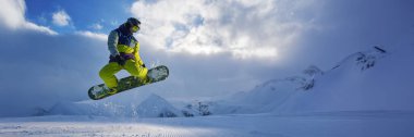 Bir snowboardcunun dinamik görüntüsü karlı bir dağ zeminine karşı, canlı renkler. Fotokopi alanı bulunan spor terfileri ve kış turizmi afişleri için ideal.