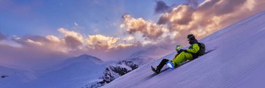 İki snowboardcu dağlarda renkli bir günbatımının tadını çıkarıyor. Canlı gökyüzü ve karlı arazi dinamik ve maceralı bir atmosfer yaratır. Spor terfileri için ideal..