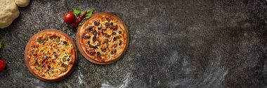 Koyu dokulu yüzeyde iki pizza, taze malzemelerle şekillendirilmiş. Zengin renkler ve bol miktarda fotokopi alanı gıda pazarlama ve restoran promosyonları için mükemmel hale getiriyor..