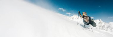 Bir snowboardcu parlak mavi bir gökyüzünün altında karlı bir dağa tırmanır. Fotokopi alanı olan geniş pankart biçimi, kış sporları veya açık hava reklamları için ideal.
