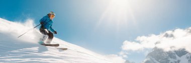 Kayakçı, fotokopi alanı olan geniş bir afiş formatında güneşli bir yamaçtan iniyor. Parlak mavi gökyüzü, dinamik hareket, kış sporları terfileri için uygun..