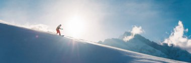 Bir snowboardcu güneşli bir yamaçtan açık mavi gökyüzüne doğru iniyor. Kış sporları promosyonları için ideal, bolca fotokopi alanı var. Canlı renkler ve aksiyon dolu.