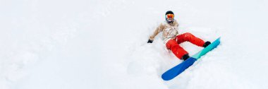 Snowboardcu karda neşeyle oturuyor. Parlak renkler, dinamik tarz. Kış sporları promosyonları ve açık hava yaşam tarzı reklamları için harika. Kopyalama alanı olan geniş pankart.