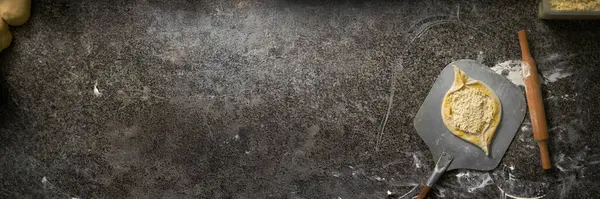 Yuvarlak pizza hamurunun siyah tezgahta merdaneli görüntüsü. Topraksı renkler ve geniş fotokopi alanı mutfak reklamları için ideal hale getiriyor. Profesyonel yemek tasarımı..