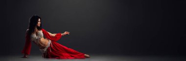 Zarif bir dansçı, arka planda kırmızı ve gümüş renkli pozlar verir. Resim dramatik, reklam ve afişler için uygun, metin için kopyalama alanı.