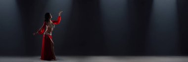 Bir kadın, karanlık bir sahnede canlı kırmızı bir elbiseyle zarif bir dans sergiliyor. Zarif poz, dramatik ışıklandırma, geniş kopya alanı. Dans ile ilgili promosyonlar için mükemmel..