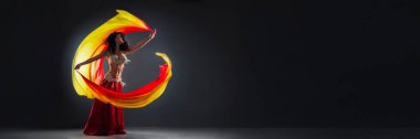 Uçan kostümlü bir dansçı karanlık bir arka planda gösteri yapıyor. Canlı renkler ve dinamik hareketler çarpıcı bir kontrast yaratır. Sanatsal ve kültürel promosyonlar için ideal.
