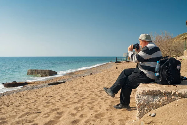 Caucasian mature photographer is taking photos on Black Sea beach in, Eastern Crimea