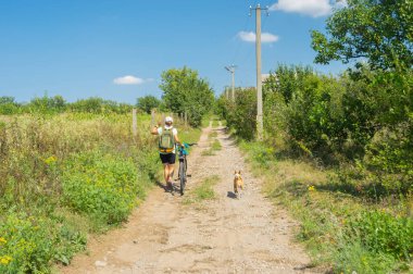 Kayalık yolda yürüyen bir kadın Basenji köpeğiyle bisiklet sürüyor Ukrayna vilasında sahibinin yanında yürüyor.