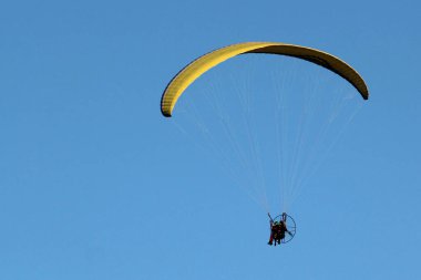 Mavi gökyüzünde paraşütle atlayan pilot motorlu uçan makineyi kontrol ediyor.