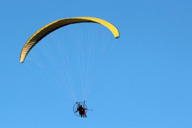 Mavi gökyüzünde paraşütle atlayan pilot motorlu uçan makineyi kontrol ediyor.