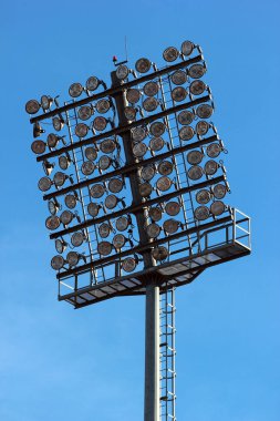 Tall lamp post, stadium light or sports lighting against blue sky background