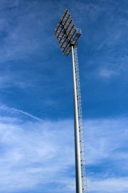 Tall lamp post, stadium light or sports lighting against blue sky background