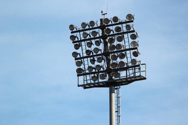 Tall lamp post, stadium light or sports lighting against blue sky background