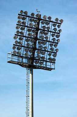 Tall lamp post, stadium light or sports lighting against blue sky background