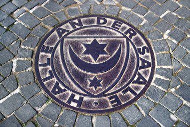 Halle, Almanya - 6 Nisan 2024: Halle, Saale, Saksonya-Anhalt şehrinin merkezindeki asfalt bir sokakta Halle armalı metal mühür