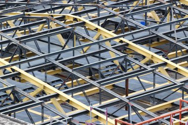 Tamamlanmamış bir çatının çelik kirişleri ve kirişleri, inşaat sahasının arkası.