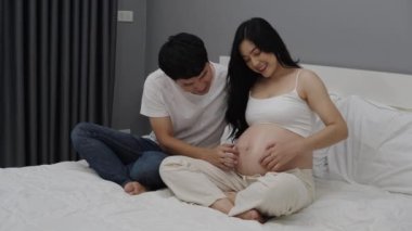 Hamile çift yatakta karnında bebekle konuşuyor ve oynuyorlar.