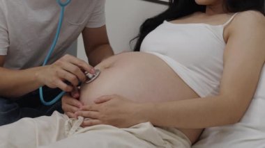 Hamile bir çiftin karnında steteskopla bebek kalp atışlarını dinlemesi.