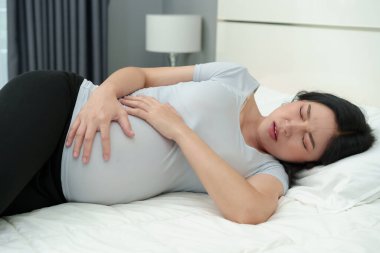 Hamile bir kadının yatakta karnı ağrıyor.