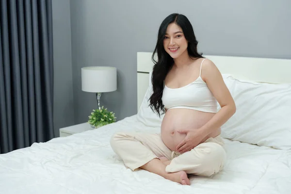 快乐的孕妇在床上抚摸着肚子 — 图库照片