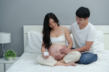 Hamile çiftin göbeğine krem sürmesi yatakta nemlendirici bir cilt için.