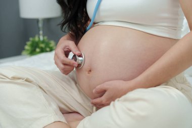 Hamile bir kadının karnında steteskopla kalp atışlarını dinlemesi.