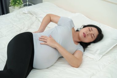 Hamile bir kadın yatakta bel ağrısı çekiyor.