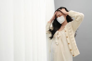 pregnant woman in medical mask for protect coronavirus (covid-19) and suffering from headache in a bedroom