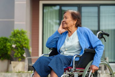stressed senior woman suffering with headache while sitting in wheelchair outside at the house