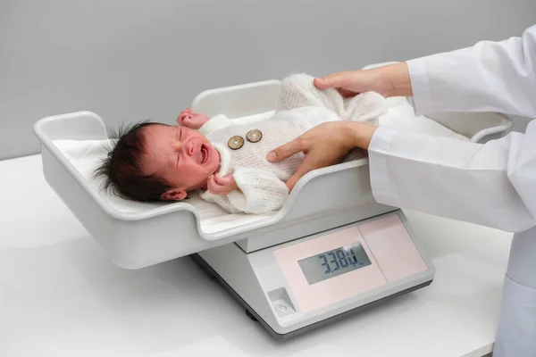 crying newborn baby weight measurement on the digital scales with doctor in hospita