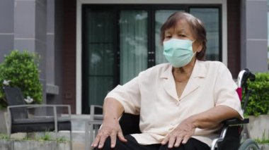 senior woman wearing medical mask for protect coronavirus (covid-19) whlie sitting in wheelchair outside at the house