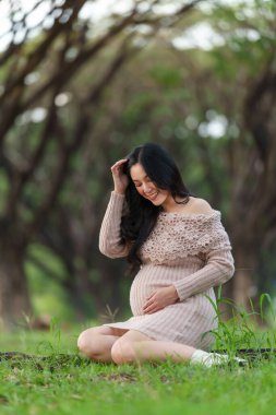 happy pregnant woman sitting and looking her belly in the park