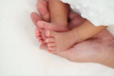 mother hand holding newborn baby feet on a bed