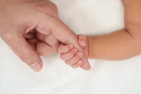 newborn baby hand holding index finger of mother on a bed