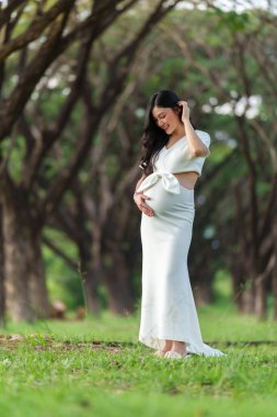pregnant woman standing and looking her belly in the park