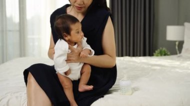 Anne sütü içtikten sonra yatak odasında geğirip ağlayan bir bebek tutuyor.