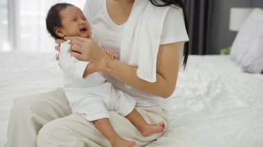 Anne sütü içtikten sonra yatak odasında geğirip ağlayan bir bebek tutuyor.