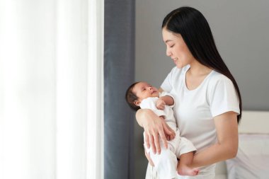 mother holding her newborn baby near the window in bedroom