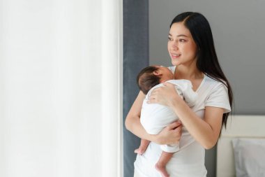 Anne yeni doğmuş bebeğini kucağında tutuyor ve yatak odasının penceresinin yanında uyuması için teselli ediyor.