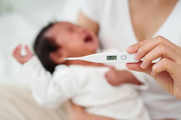 mother measuring temperature of ill and crying baby. sick child with high fever on a bed