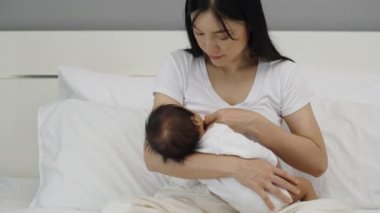 Anne, yeni doğan bebeği yatakta emziriyor.